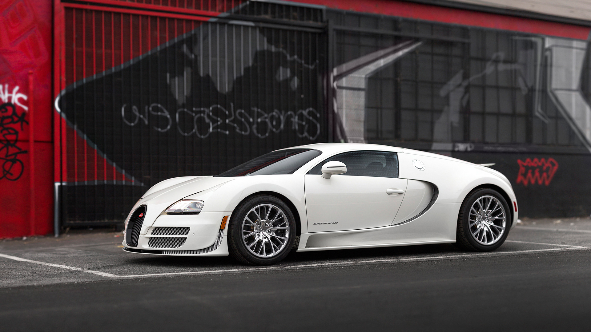 Белый Bugatti Veyron стоит на фоне черно-красной стены