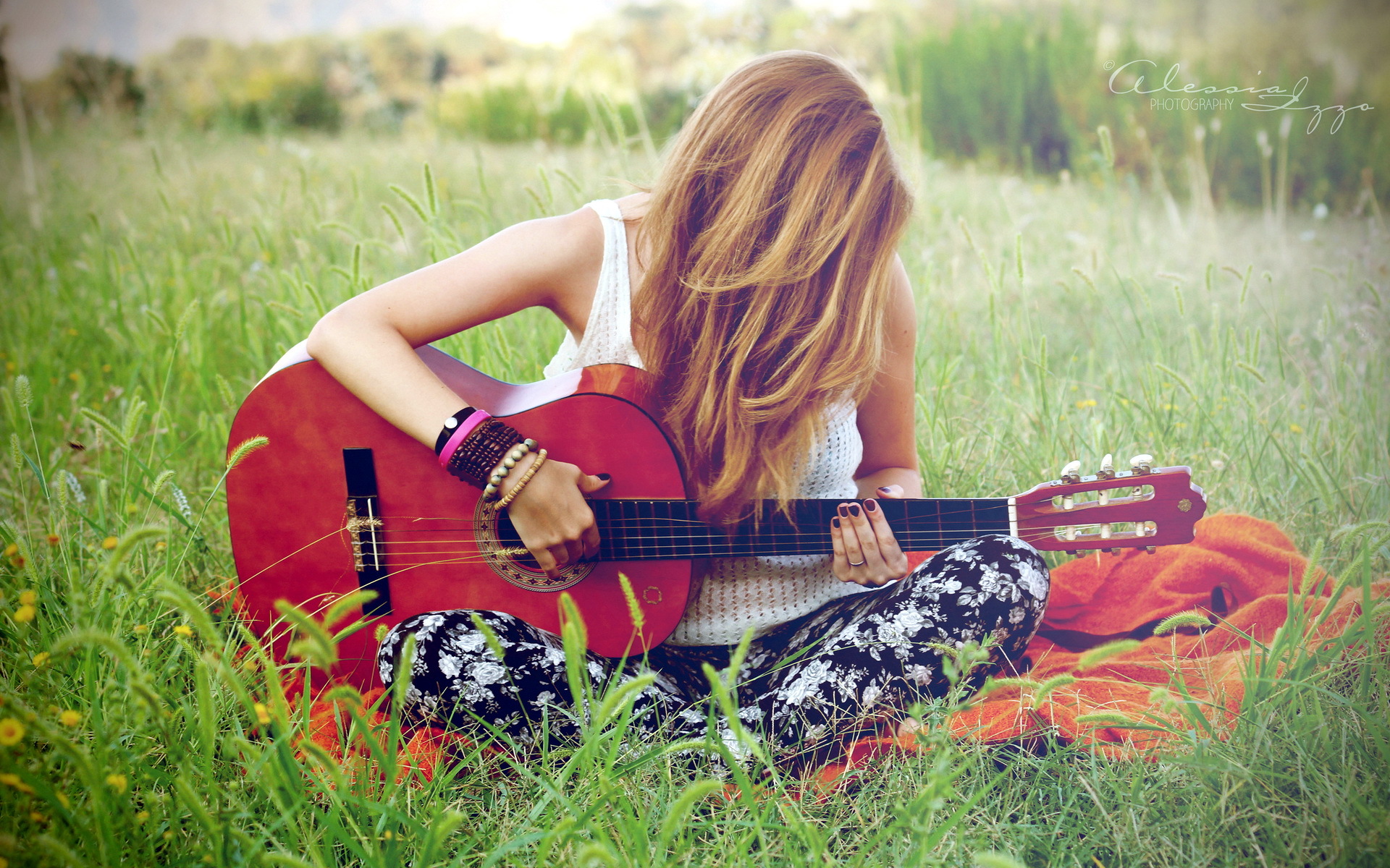 Девушка с гитарой сидит на лугу
