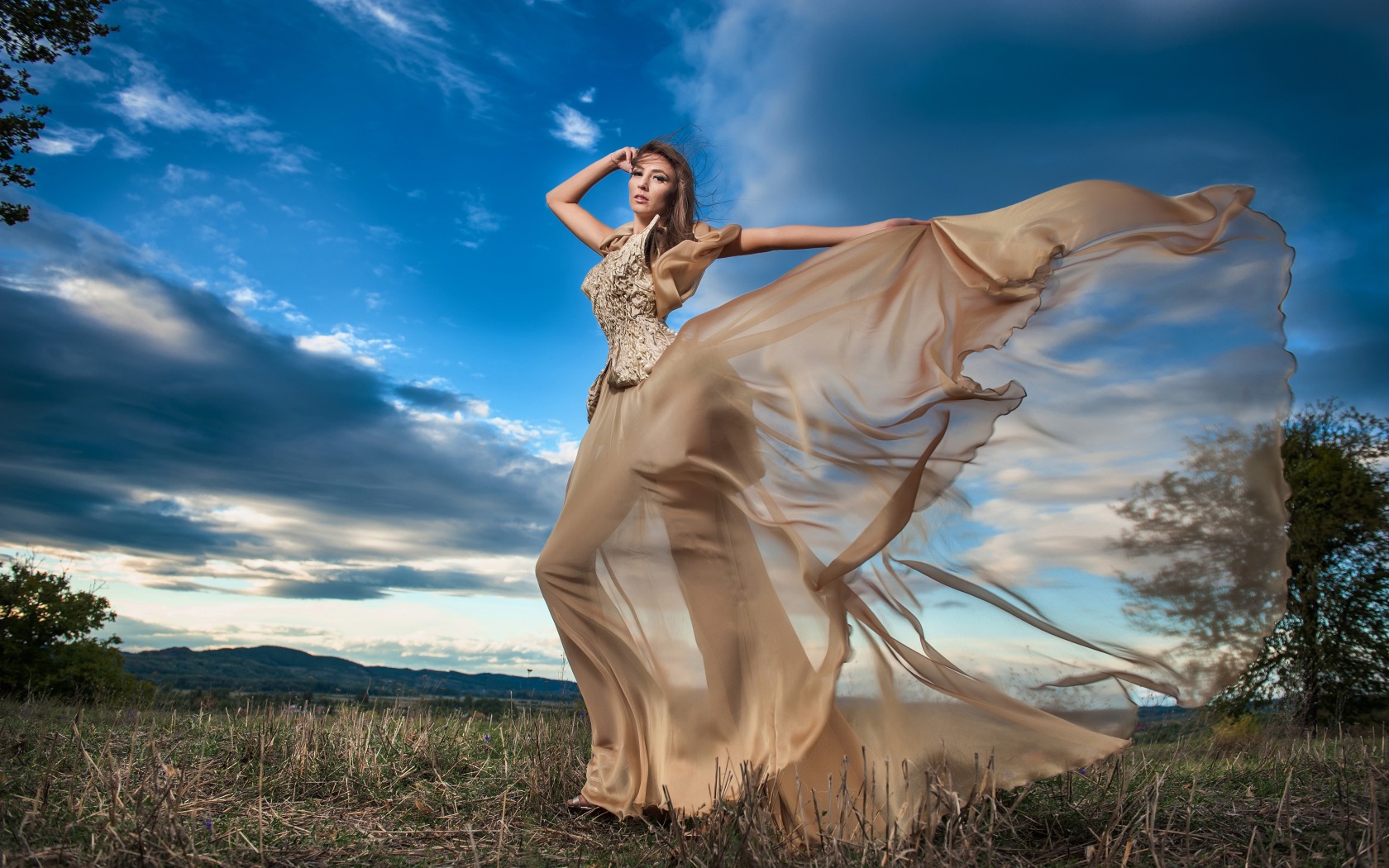 Девушка в красивом платье стоит в поле на фоне голубого неба