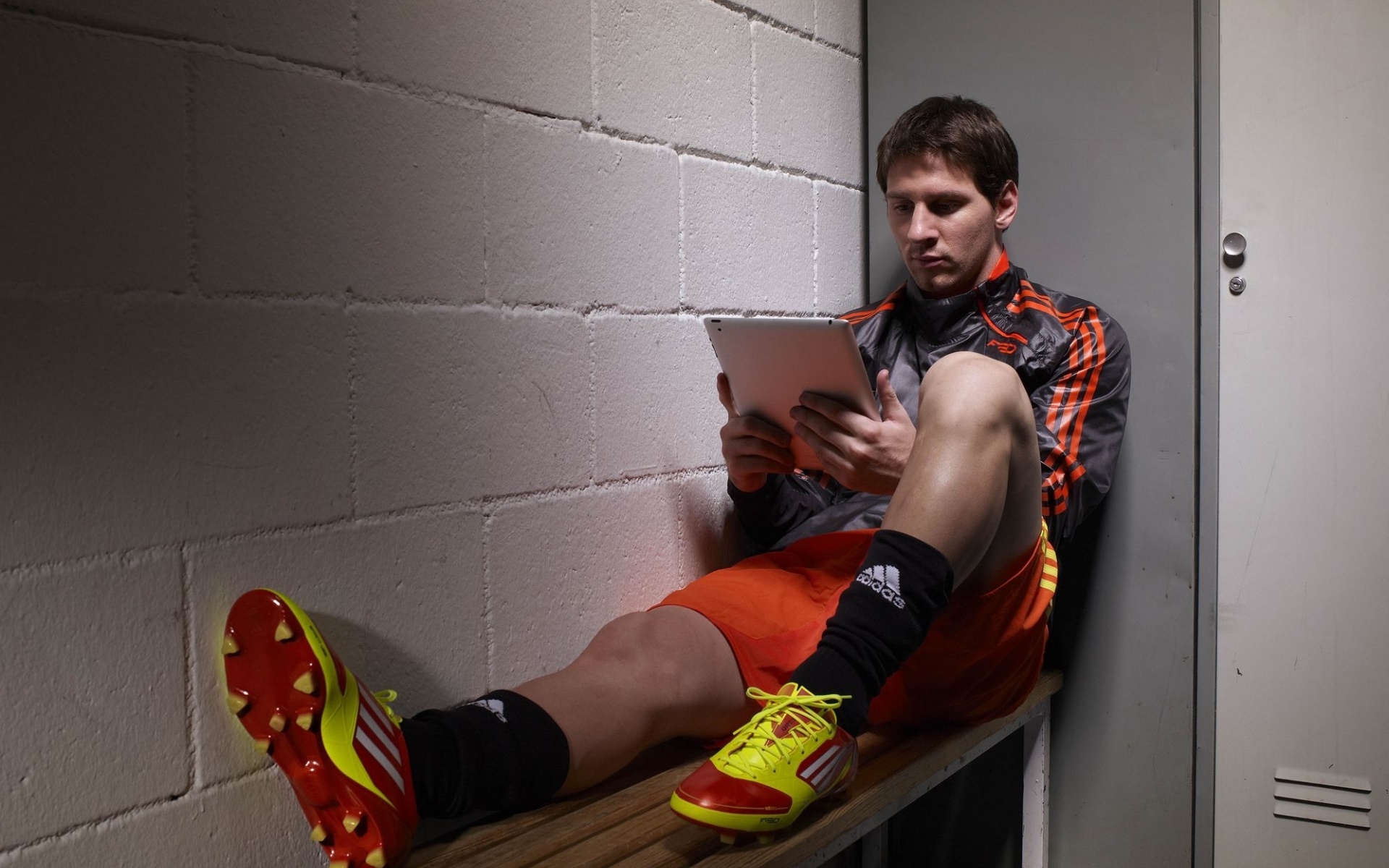 Известный футболист Лионель Месси / Lionel Messi сидит с планшетом в руках на лавке в раздевалке