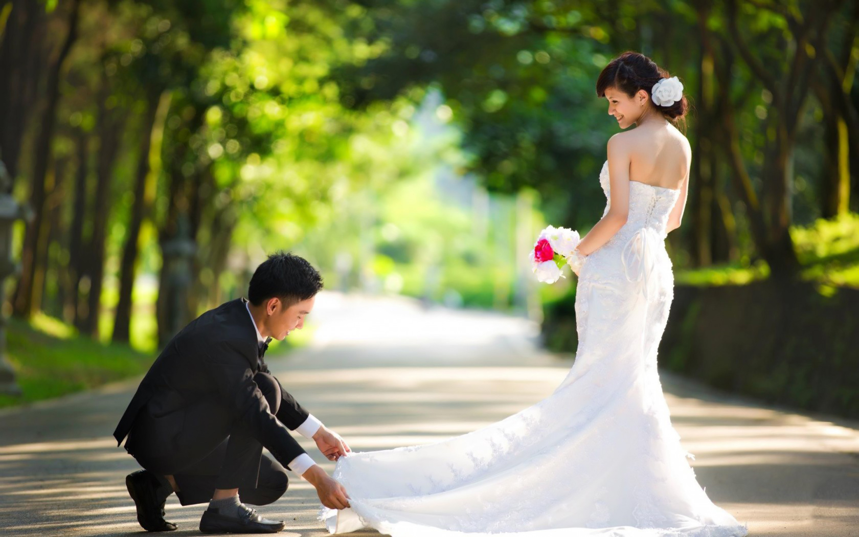 Жених поправляет невесте подол платья на дорожке в парке