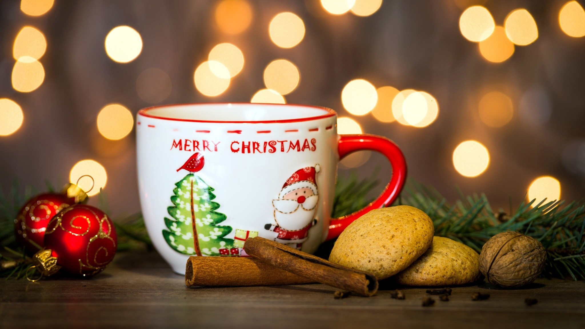 Кружка с надписью Merry Christmas / Веселого Рождества, печенье, палочки корицы и новогодние шарики на столе на фоне боке