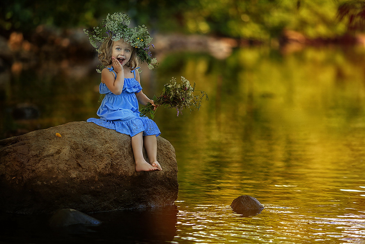Милая, светловолосая, улыбающаяся девочка в синем легком сарафане с венком на голове из полевых цветов, держащая в руке такой же небольшой букетик