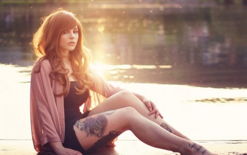 Девушка с татуировками на ногах сидит возле речки