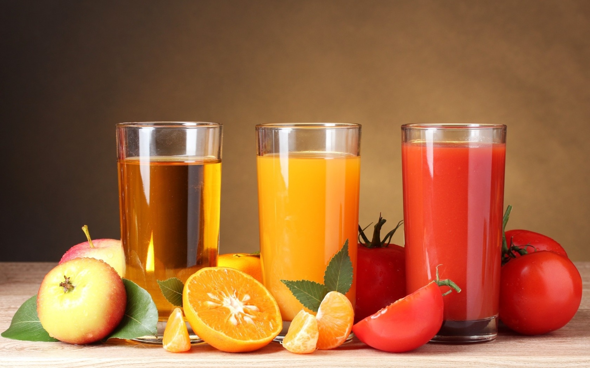 Три стакана с апельсиновым, яблочным и томатным соками на столе