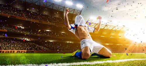 Футболист празднует победу на стадионе, стоя на коленках, надев футболку на голову и вскинув руки вверх