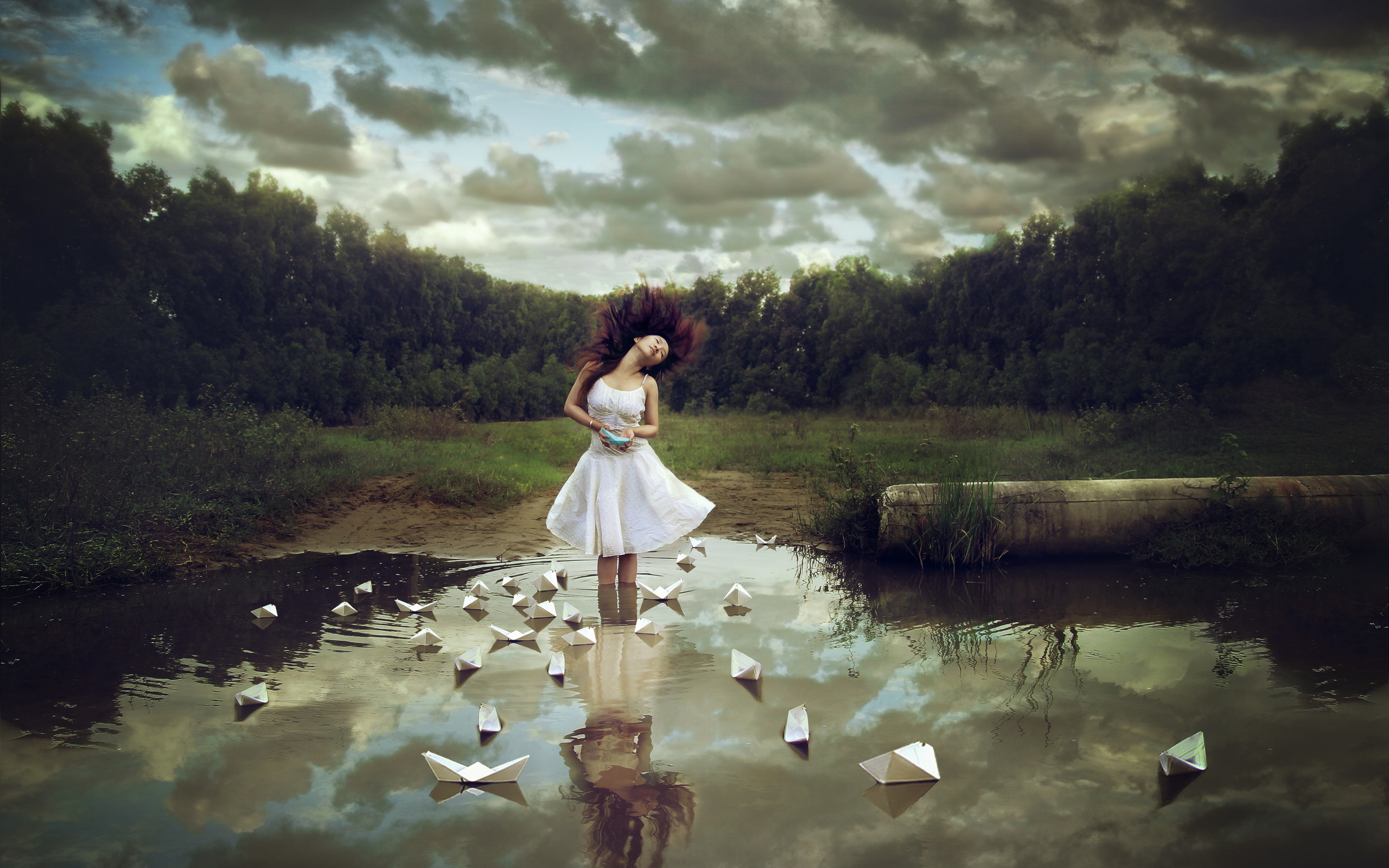 Девушка - азиатка стоит в воде на фоне леса, в которой плавают бумажные кораблики