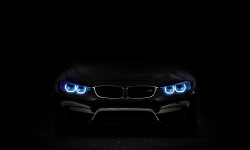 Черный автомобиль BMW с ярко-синими светодиодными фарами стоит, демонстрируя свою переднюю часть на черном фоне