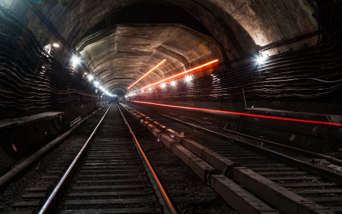 Железнодорожные в тоннеле метро, освещенном боковыми светильниками, с длинными красными следами света от проходящего поезда