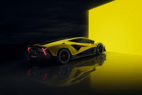 Желтый с черными элементами спорткар Lamborghini Fenomeno с красными фарами стоит на отражающем темном полу, на фоне светящейся желтой стены