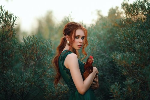 Модель Anna Churakova в зеленом платье и с курочкой в руках стоит среди кустов на природе