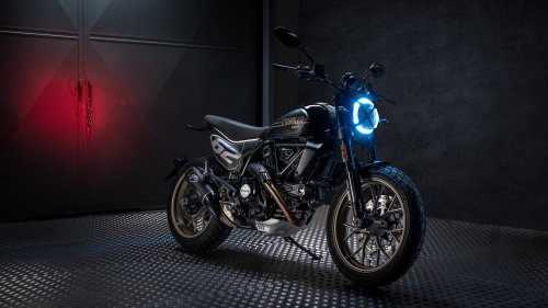 Мотоцикл Ducati Scrambler черного цвета с ярко-синей круглой фарой стоит на металлической поверхности на темном фоне с красным свечением