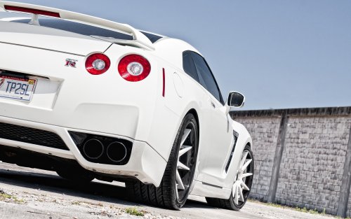 Белый Nissan GTR на асфальте, на фоне бетонной стены и голубого неба