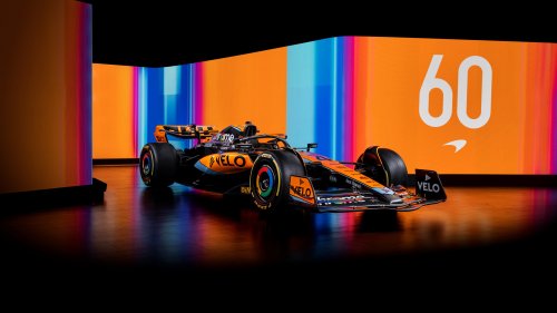 McLaren F1 гоночный автомобиль черного и оранжевого цвета на темном полу, (VELO, chrome) на фоне светящихся панелей с оранжевыми и синими полосами