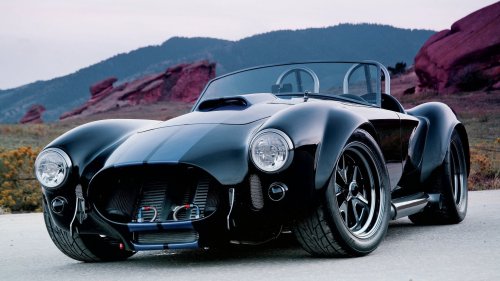Черный автомобиль Ac Cobra / Shelbi с синими полосами припаркован на дороге, на фоне гор с красными скалами