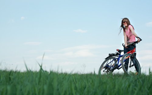 Девушка держится, улыбаясь, за свой велосипед