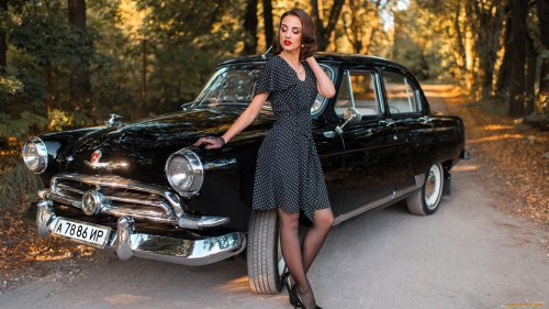 Девушка в ретро платье черного цвета в белый горошек, черные туфли и черные прозрачные перчатки стоит облокотившись на автомобиль ГАЗ-21 Волгa