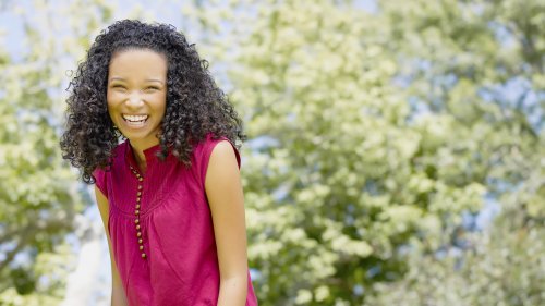 Красивая чернокожая девушка в розовом платье смеется под деревьями
