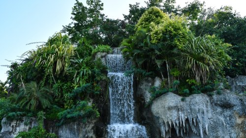 Многоуровневый водопад окруженный густой тропической растительностью и деревьями, на фоне светлого неба