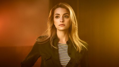 Портрет Brianne Howey / Брианны Хоуи, которая смотрит в сторону, в зеленой куртке и полосатой футболке, на фоне оранжево-коричневого градиента