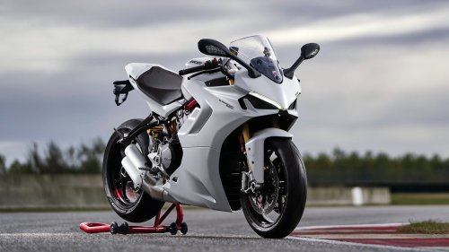 Белый мотоцикл Ducati / Дукати SuperSport / СуперСпорт 950 / 950 S / С на красной подставке на асфальте гоночной трассы на фоне размытых деревьев