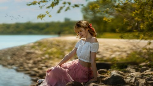 Модель Аля в светлой блузке и в розовой юбке сидит на берегу водоема