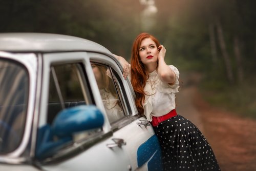 Рыжеволосая девушка в светлой блузке и в юбке в горошек стоит на лесной дороге у авто Волга ГАЗ 21